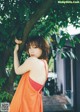 A woman in an orange dress leaning against a tree.